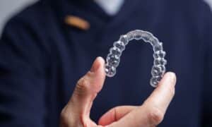 Person holding a clear Invisalign® aligner, demonstrating how it helps to straighten teeth. The background is slightly blurred, focusing attention on the aligner.